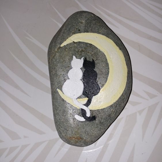 painted rock that has moon and white and black cat snuggling on it